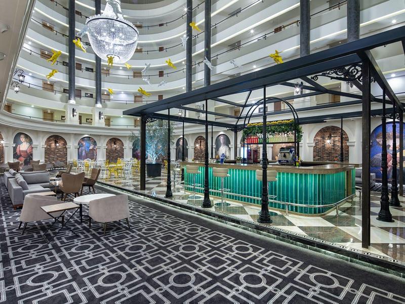 Elegante hotellounge met ronde zitgedeeltes, tapijtvloer en groen verlichte bar.