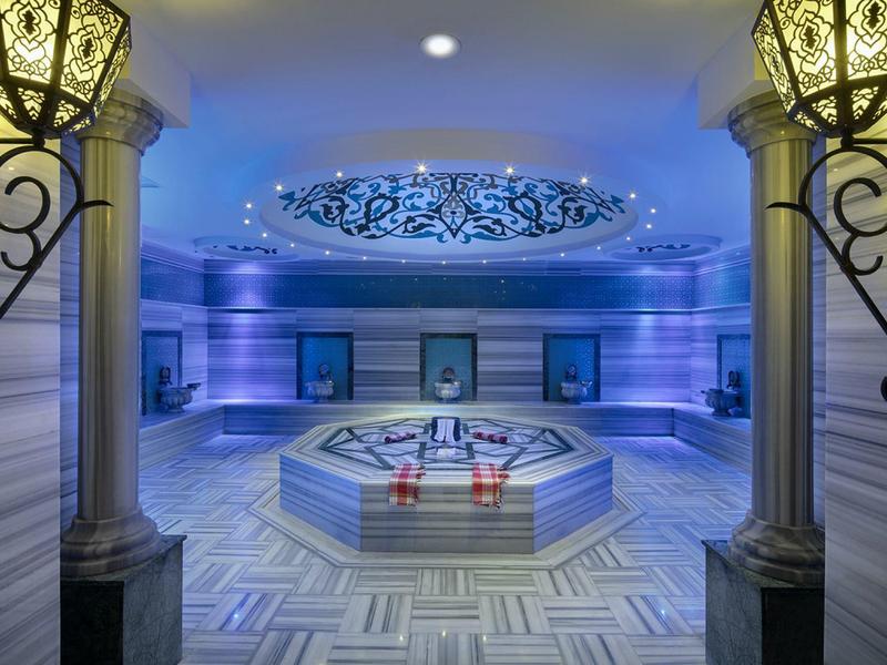 Luxe verlichte stoomkamer met centrale marmeren fontein en decoratief plafondelement.