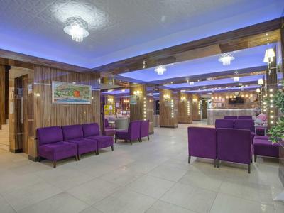 Großer, moderner Warteraum mit lila Sofas, warmem Licht und hellen Fliesenboden.