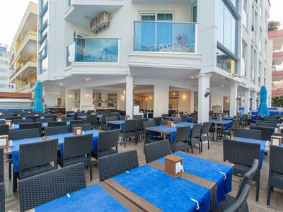 Außenbereich eines Restaurants mit vielen Tischen, blauen Tischdecken und Stühlen aus Rattan.