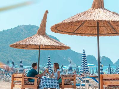 Strand met strooien parasols en mensen op houten ligstoelen, bergen op de achtergrond