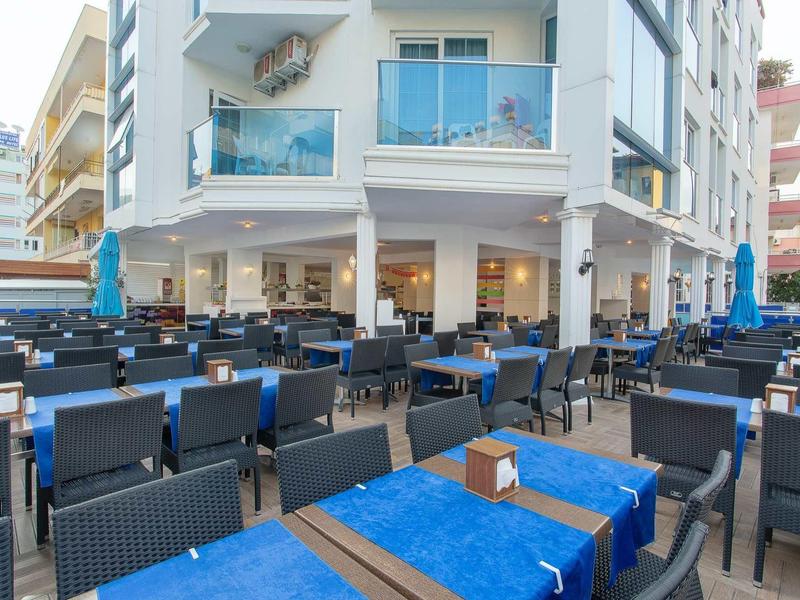 Außenbereich eines Restaurants mit vielen Tischen, blauen Tischdecken und Stühlen aus Rattan.