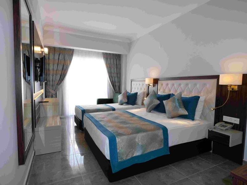 Modernes Schlafzimmer mit großem Bett, blauen Akzenten und Fenster mit Gardinen, heller Raum.