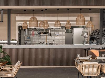 Moderní restaurace s ratanovými židlemi a otevřenou kuchyní v pozadí.