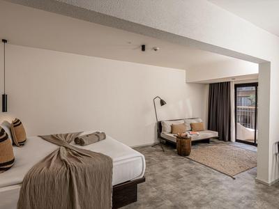 Moderní hotelový pokoj s manželskou postelí, posezením, kobercem a přístupem na balkon.