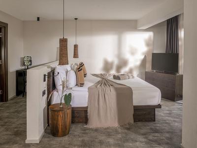 Moderní hotelový pokoj s manželskou postelí, kobercem a minimalistickým zařízením v neutrálních tónech.