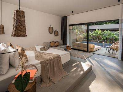 Moderně zařízený hotelový pokoj s velkými pohovkami, denním lůžkem a francouzskými okny s výhledem do zahrady.