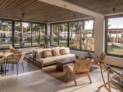 Moderní obývací pokoj s velkými okny, světlou pohovkou a dřevěnými židlemi s výhledem na zahradu