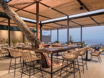 Otevřená jídelna s dřevěnou střechou a výhledem na moře, s moderními stoly a židlemi.