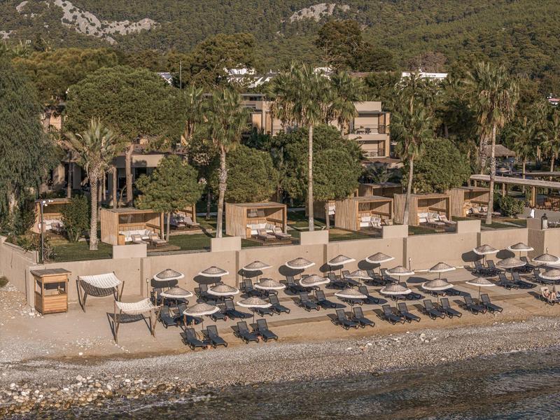 Pláž s lehátky a altánky před zalesněnými kopci v pozadí.