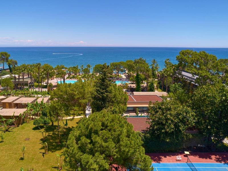 Pohled na hotelový resort s zelení, stromy a mořem v pozadí za jasného počasí