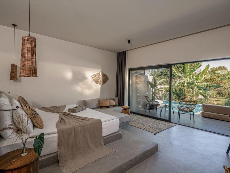 Moderní hotelový pokoj s manželskou postelí, terasou a výhledem na tropické rostliny.