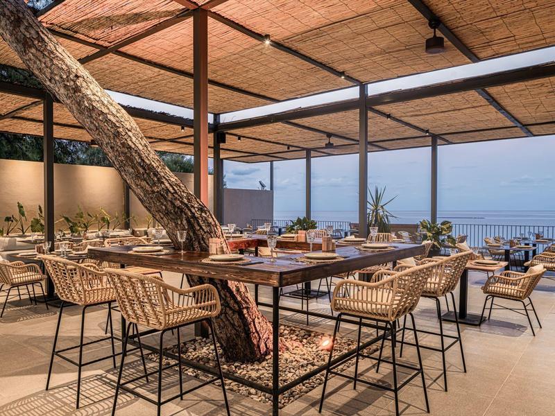 Otevřená jídelna s dřevěnou střechou a výhledem na moře, s moderními stoly a židlemi.