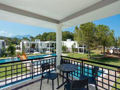Balkon mit Tisch und Stühlen, Blick auf Pool, grüne Rasenflächen und moderne weiße Gebäude.