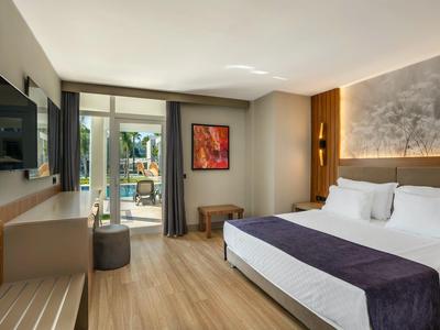 Modernes Hotelzimmer mit Doppelbett, großem TV, Holzfußboden und Zugang zu Balkon mit Sitzmöbeln.