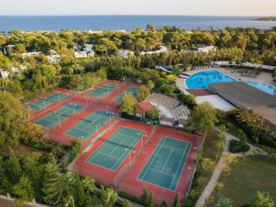 Veduta aerea di un resort con campi da tennis e piscina in una zona verde vicino al mare.