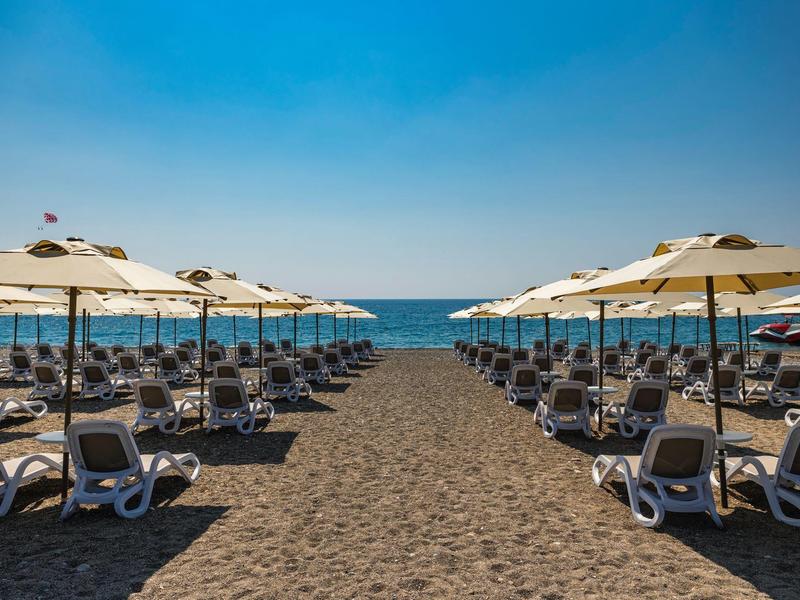 Strand mit Reihen von weißen Liegestühlen und Sonnenschirmen vor blauem Himmel und Meer.