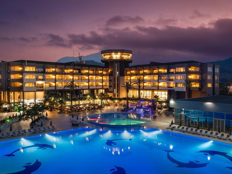 Modernes Hotel bei Dämmerung mit beleuchtetem Pool und Bergen im Hintergrund.