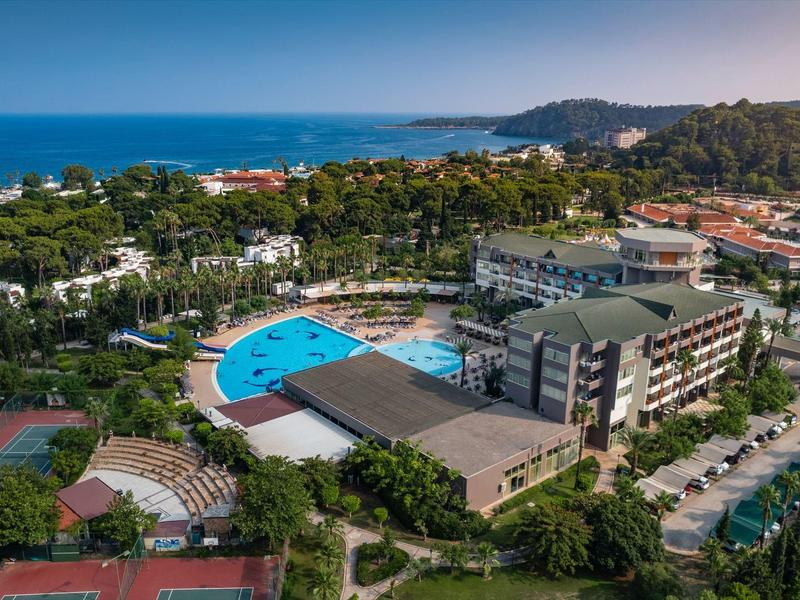 Luftaufnahme eines Resortkomplexes mit Pool, Tennisplätzen und angrenzendem Meer im Hintergrund.