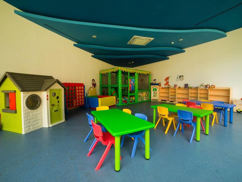 Kleurige speeltuin voor kinderen met tafels, stoelen, speelhuis en speelgoed in felle primaire kleuren.