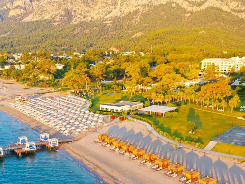 Strandhotel met parasols, ligstoelen, pier en bergen op de achtergrond onder een heldere lucht.