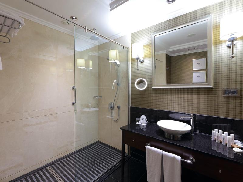 Moderne hotelbadkamer met glazen douche, donker meubel, witte wastafel en verlichte spiegel.