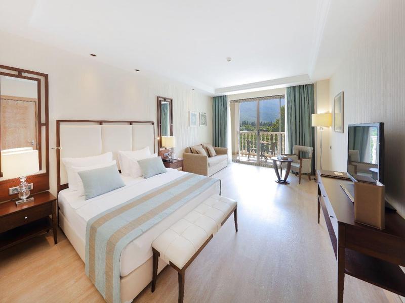 Lichte hotelkamer met twee eenpersoonsbedden, zithoek, groot raam en balkon met uitzicht op groen.