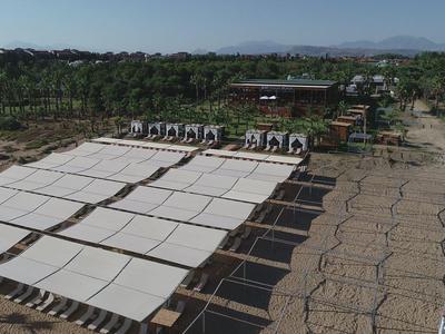 Groot schaduwrijk gebied met witte zonnetenten naast een groene tuin en hutten.