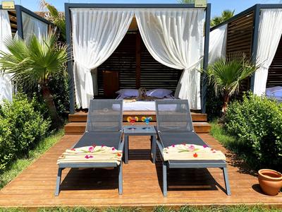 Twee ligstoelen met handdoeken voor een overdekte cabana met witte gordijnen.