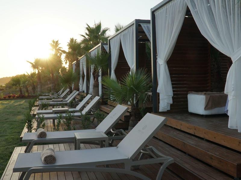 Rij ligstoelen en cabana's met witte gordijnen buiten bij zonsondergang.