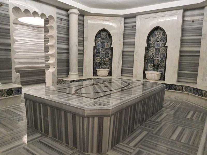 Elegante hamam met grijze marmeren muren, zuilen en centrale wasruimte.