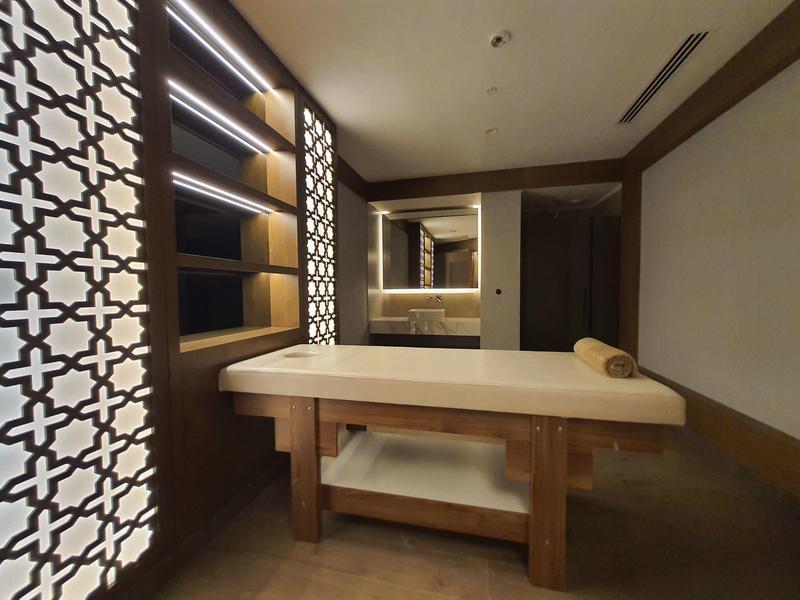 Modern ingerichte massageruimte met verlichte wand en massagetafel.