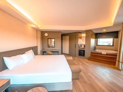 Habitación de hotel luminosa con cama grande, suelo de madera y zona de asientos con ventanal.