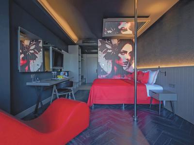 Modern hotel room with red accents, wall art, and dark wooden flooring.