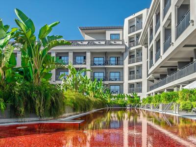 Complejo hotelero moderno con una piscina de agua roja y exuberante vegetación tropical.