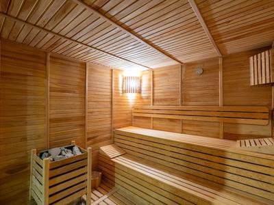 Sauna acogedora de madera clara con bancos de varios niveles y estufa iluminada.