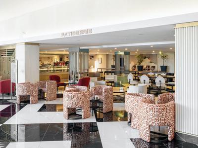 Área de comedor de hotel luminosa con sillas estampadas y suelo a cuadros en blanco y negro.