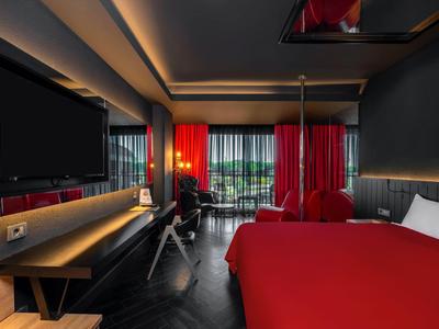 Camera d'hotel moderna con accenti rossi, letto grande, TV e vista sul balcone.