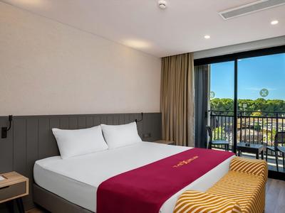 Camera d'hotel moderna con letto grande, balcone e vista sul verde.