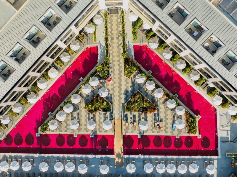 Vista aérea de una piscina de hotel con tumbonas rojas y plantas verdes en el patio interior.