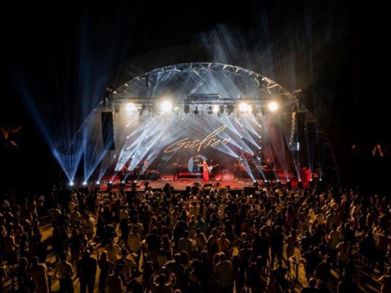 Gran multitud frente a un escenario iluminado por la noche en un evento.