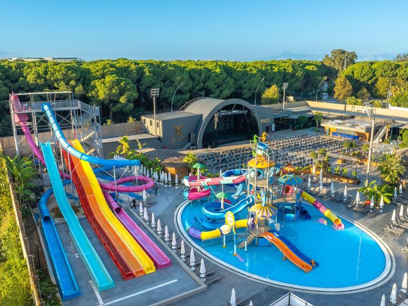 Colorido parque acuático con varios toboganes y una gran piscina, rodeado de árboles.