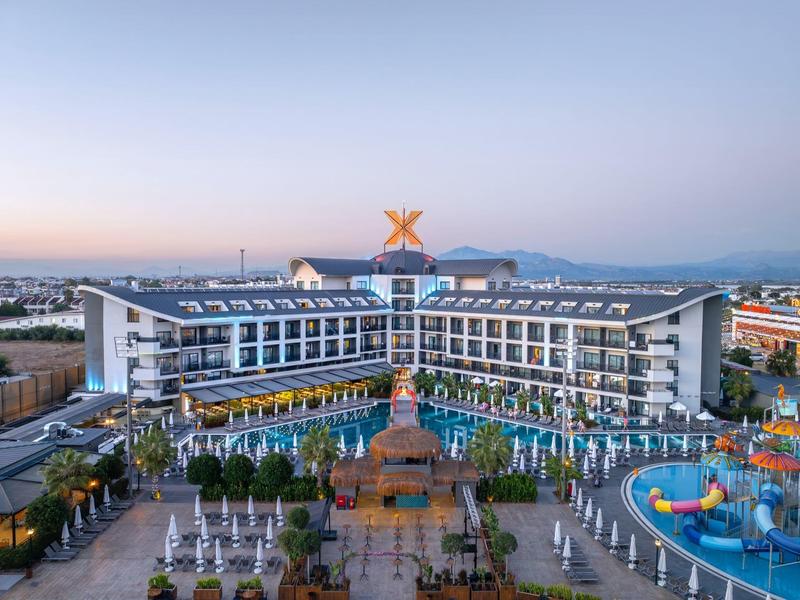 Hotel resort moderno con piscinas, tumbonas y parque acuático al atardecer