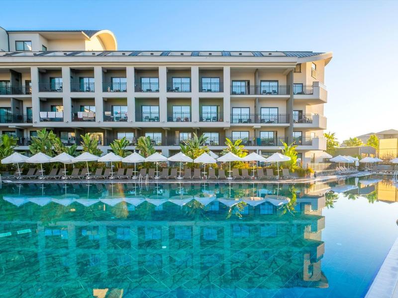 Hotel moderno con habitaciones con balcón y gran área de piscina bajo la luz del sol.