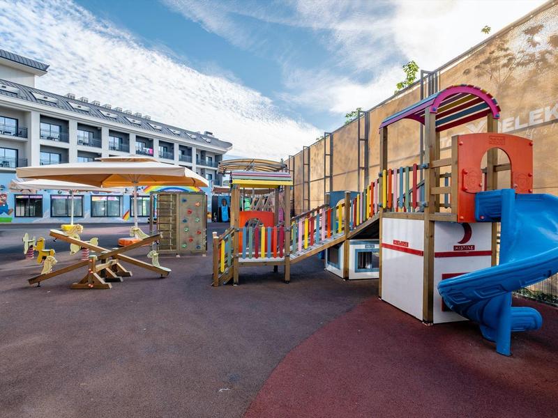 Parque infantil moderno con toboganes y columpios en el patio de un hotel bajo un cielo azul