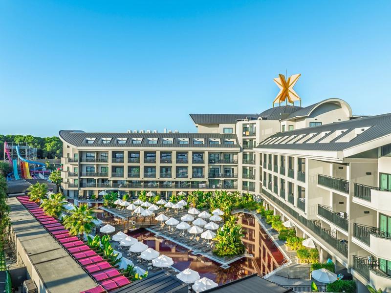 Moderní hotel s několika patry, slunečníky a zelení za slunečného dne.