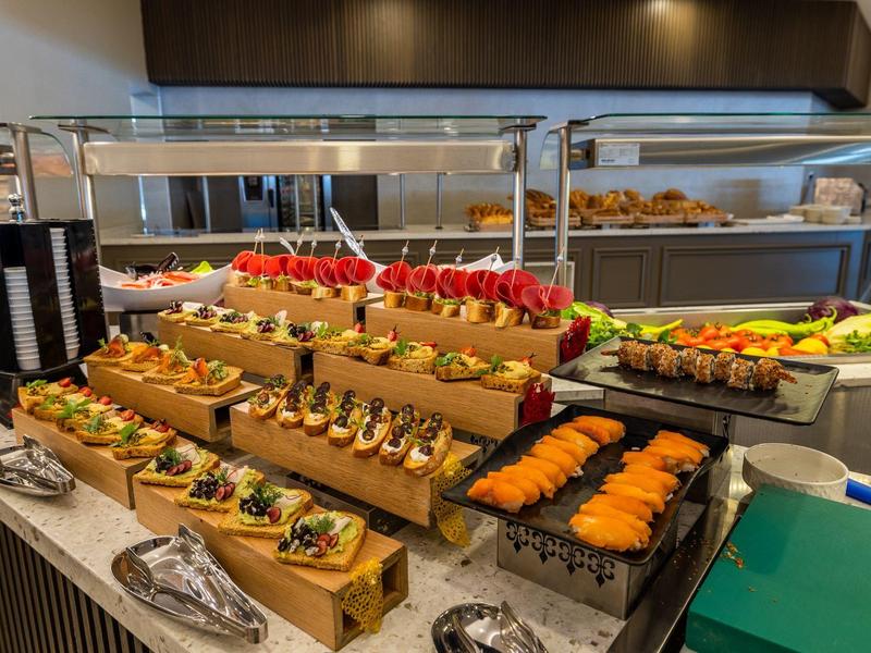 Buffet con variedad de panes con toppings, salmón y diferentes aperitivos presentados en bandejas de madera.