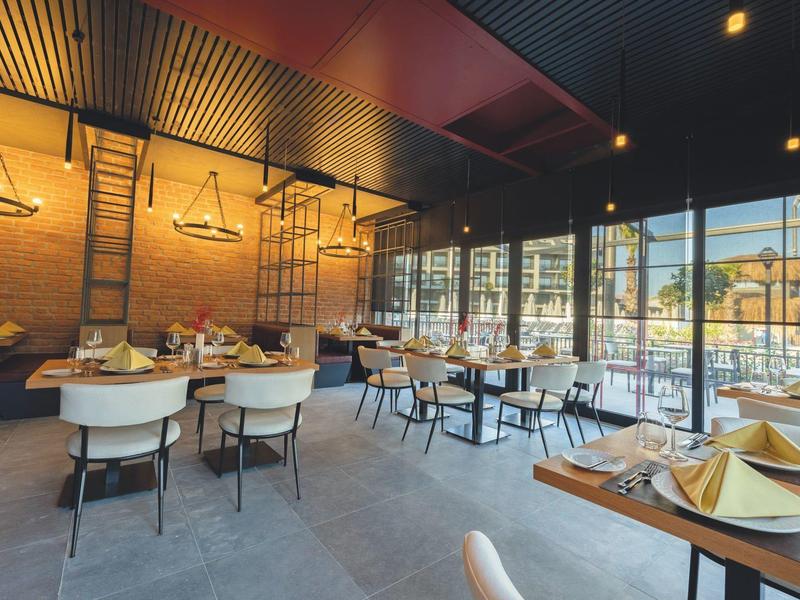 Restaurante moderno con grandes ventanales y mesas preparadas con servilletas cerca de un hotel o resort.