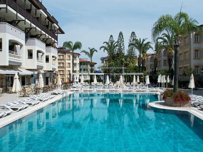 Groot zwembad met witte ligstoelen en omringende meerlaagse hotels onder een heldere lucht
