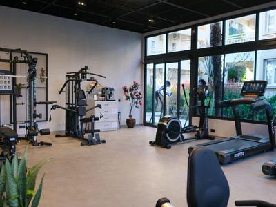 Moderne fitnessruimte met apparatuur en grote ramen met uitzicht op een binnenplaats.